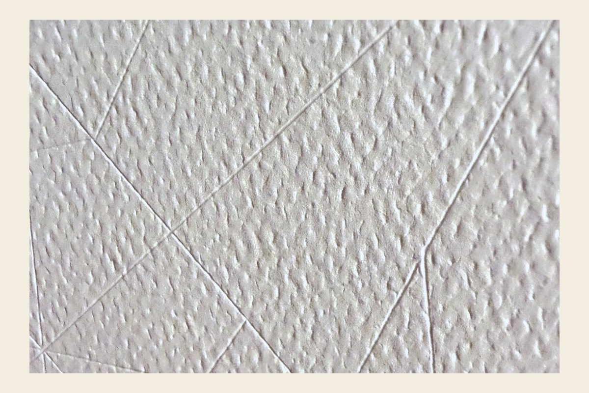A close-up of score lines pressed into textured white paper, lit from the side